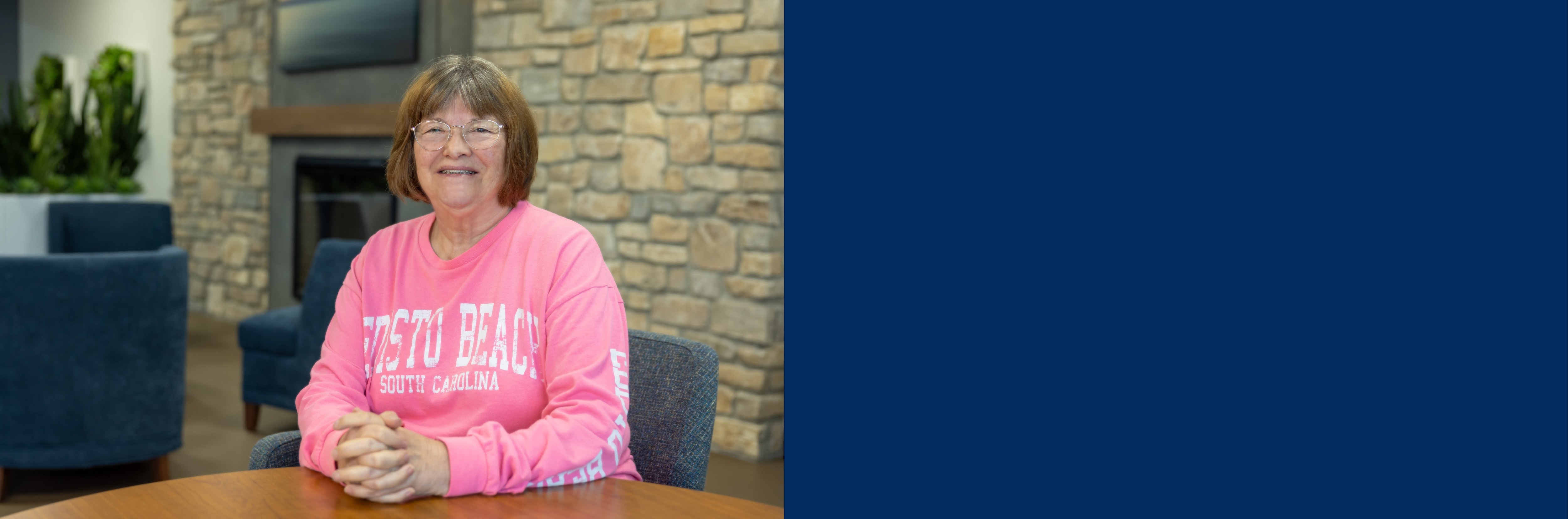 Photo of Patsy Deveney smiling at the camera in front of a fireplace.