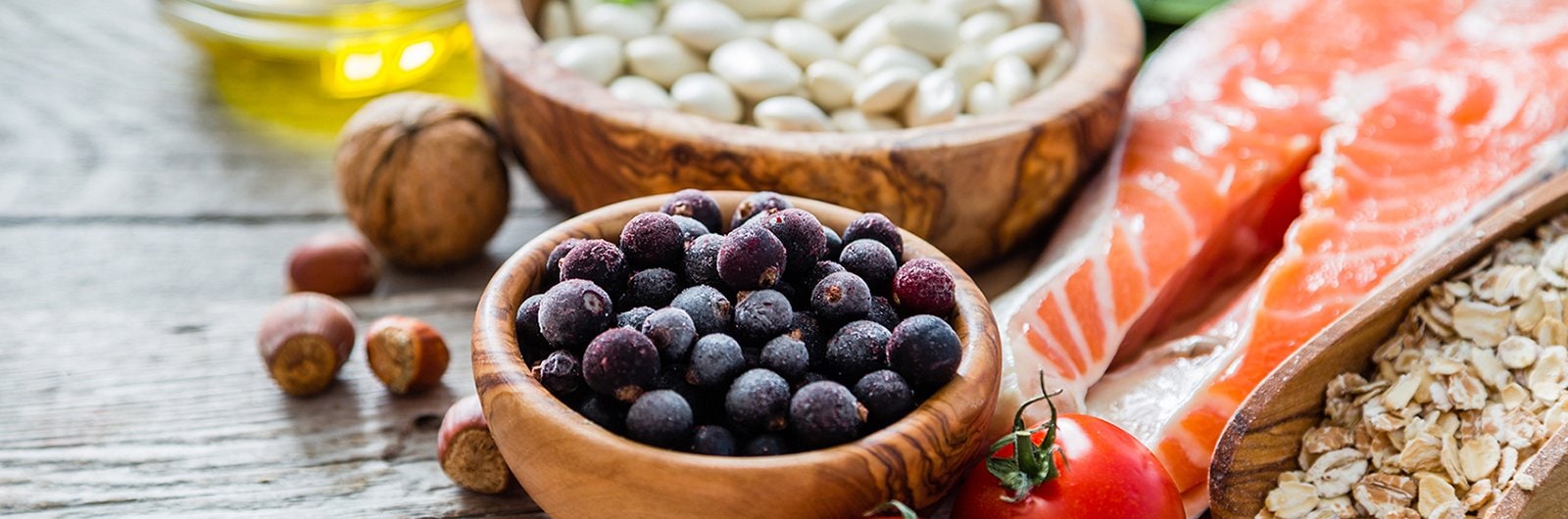 Photo of fresh food including berries, dried beans, oatmeal and fish, displayed on a wooden board. 