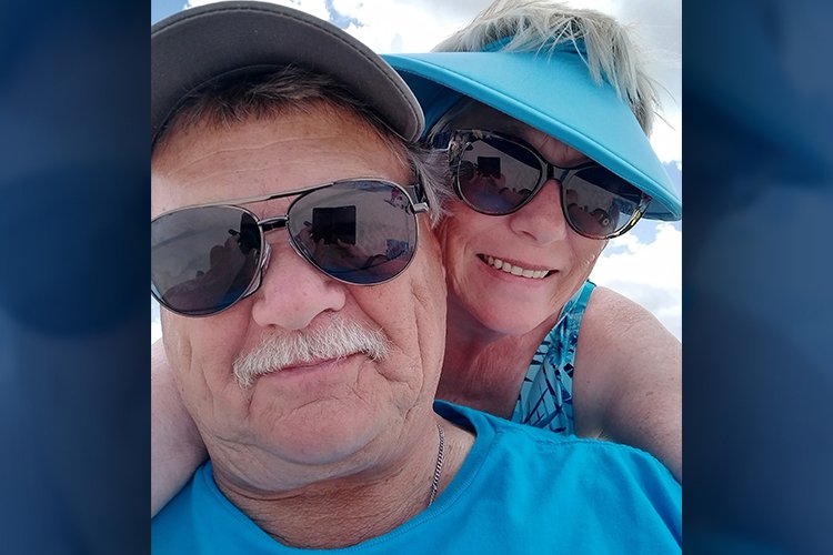 Photo of Terry Geary and husband, Bob, outdoors with sunshine and clouds behind them.