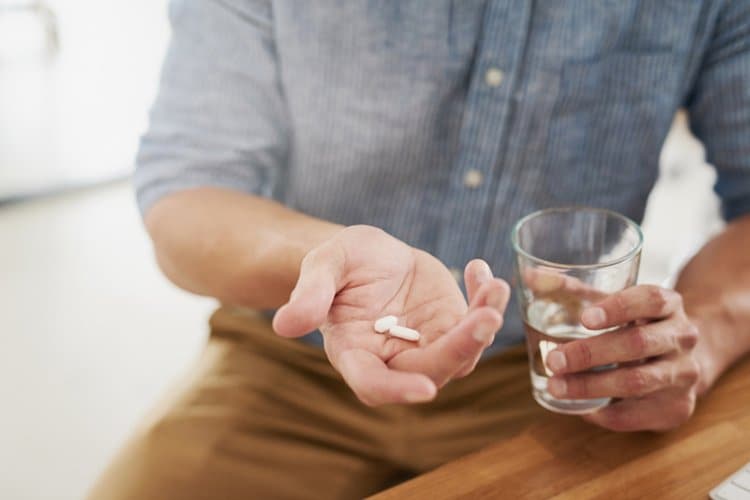 Image of a man holding pills in his hand.