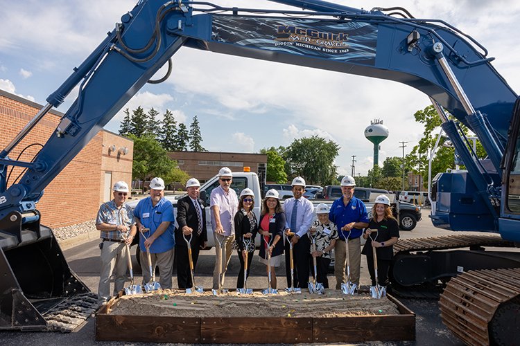 Group shot with people wearing hard hats and holding shovels digging in the sand.