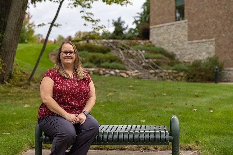 Photo of Tammy Potter sitting on park bench outside Gerstacker Building. 