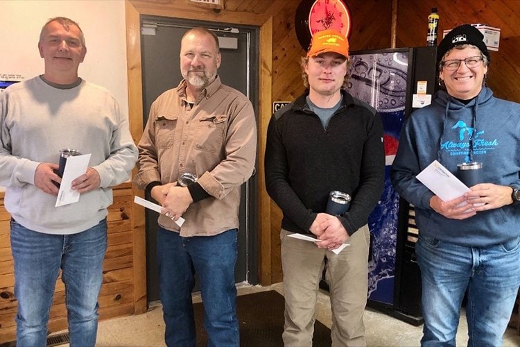 Group photo of four men holding their prizes from the clay shoot.