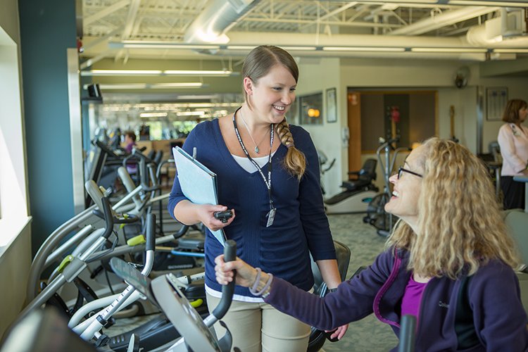 Photo of a physical therapist with a patient on an exercise bike.