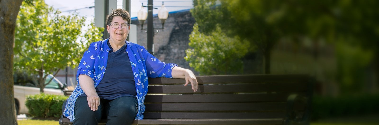 Photo of Pamela Brunn sitting on a park bench on a warm sunny day.