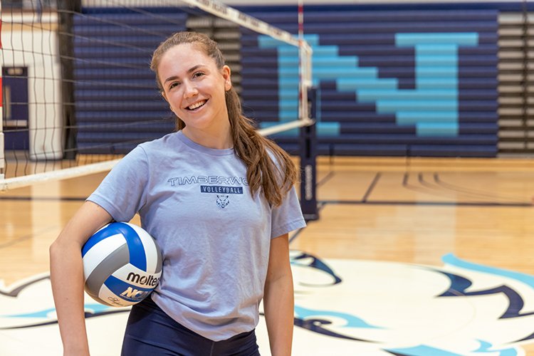 Photo of Venera Kadriu holding a volleyball and standing next to a volleyball net at Northwood University.