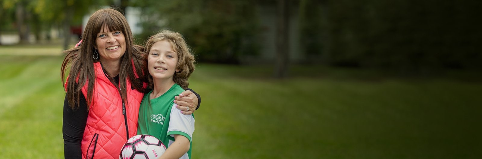 Debbie Mauer and a child soccer player, standing outside hugging each other.