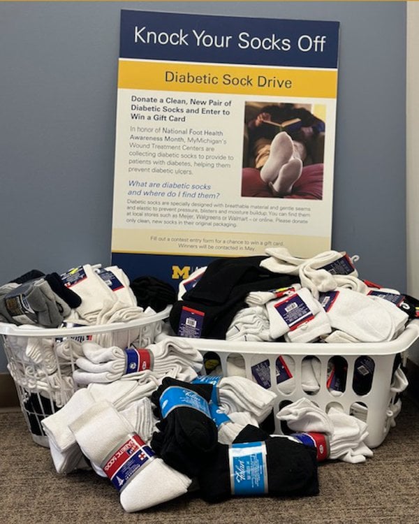 Photo of two laundry baskets overflowing with donated diabetic socks. A sign behind the baskets reads "Knock Your Socks Off. Diabetic Sock Drive. Donate a clean, new pair of diabetic socks and enter to win a gift card."