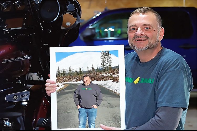 Nathan Everset holding a photo of himself pre-bariatric surgery, by a motorcycle