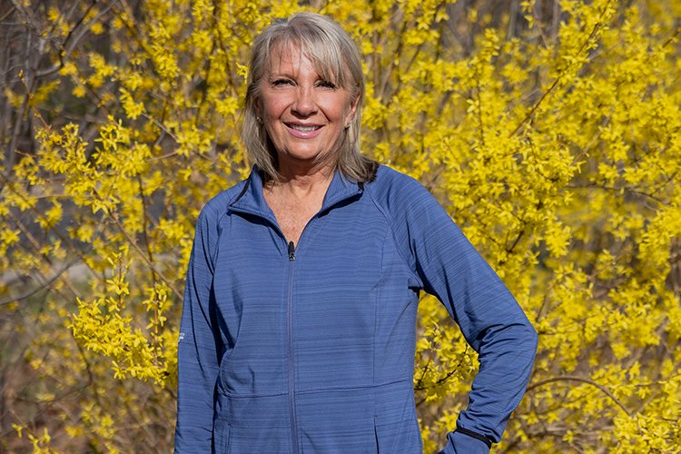 Photo of Sandy Meyer standing in front of yellow trees, smiling. 