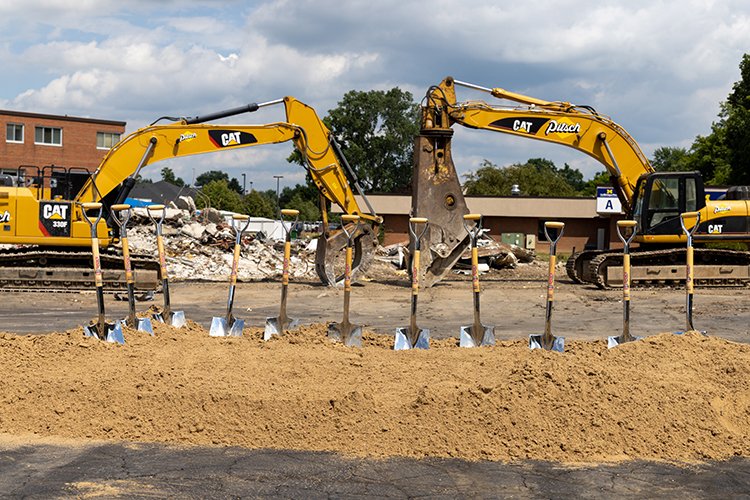 Photo of two excavators lined up front-to-front in front to the demolition project with 11 shovels stuck in the sand in front of the excavators.