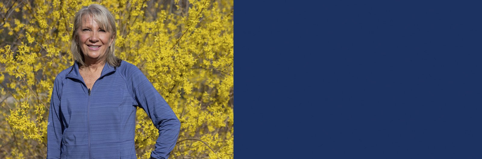 Photo of Sandy Meyer standing in front of yellow trees, smiling.