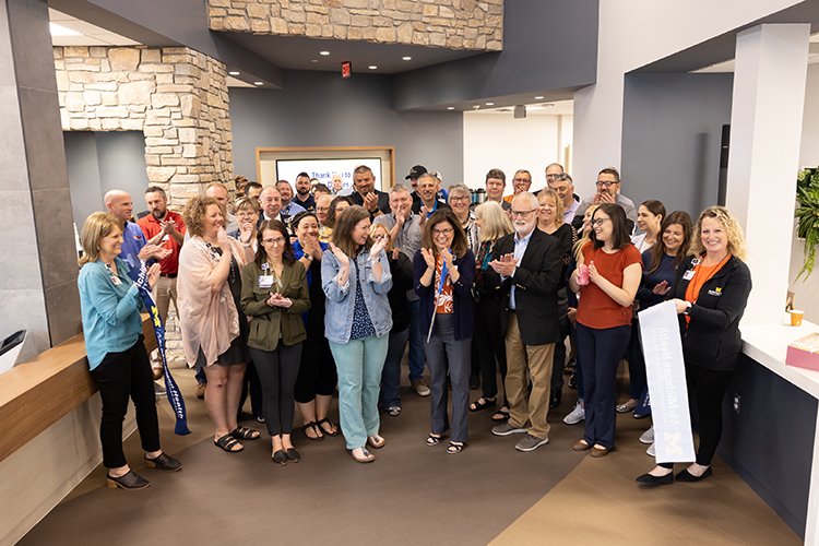 Group photo of people clapping and smiling at the ribbon cutting inside new entrance.