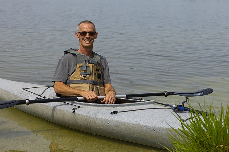 Photo of Jeff Lumsden in a kayak on the water, wearing a life vest and holding a paddle.