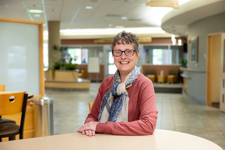 Heidi Kolb, sitting at a table with hands folded, smiling for the camera.