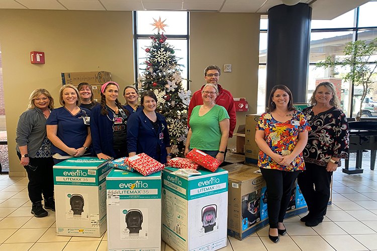 Photo of staff with car seats near a Christmas Tree.