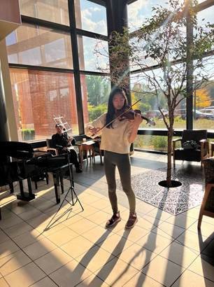 Photo of Madeline Cha playing the violin in front of sunny windows.